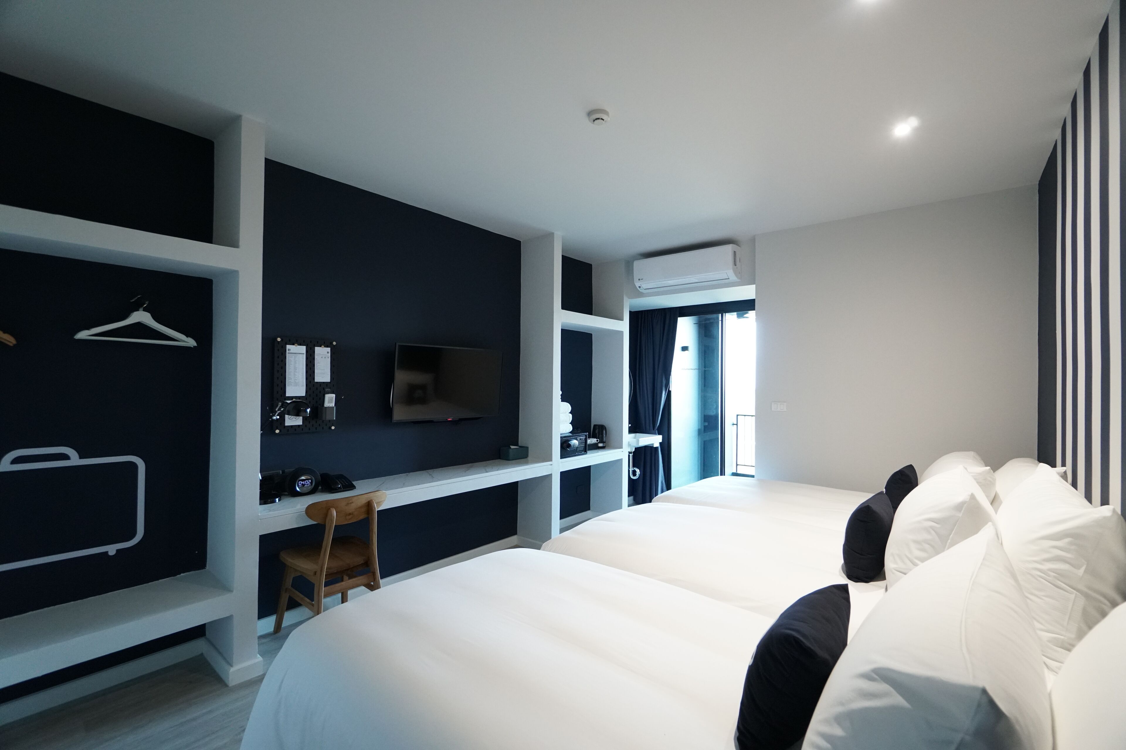Een moderne hotelkamer met twee tweepersoonsbedden, een bureau met stoel, een televisie en een kledingkast.