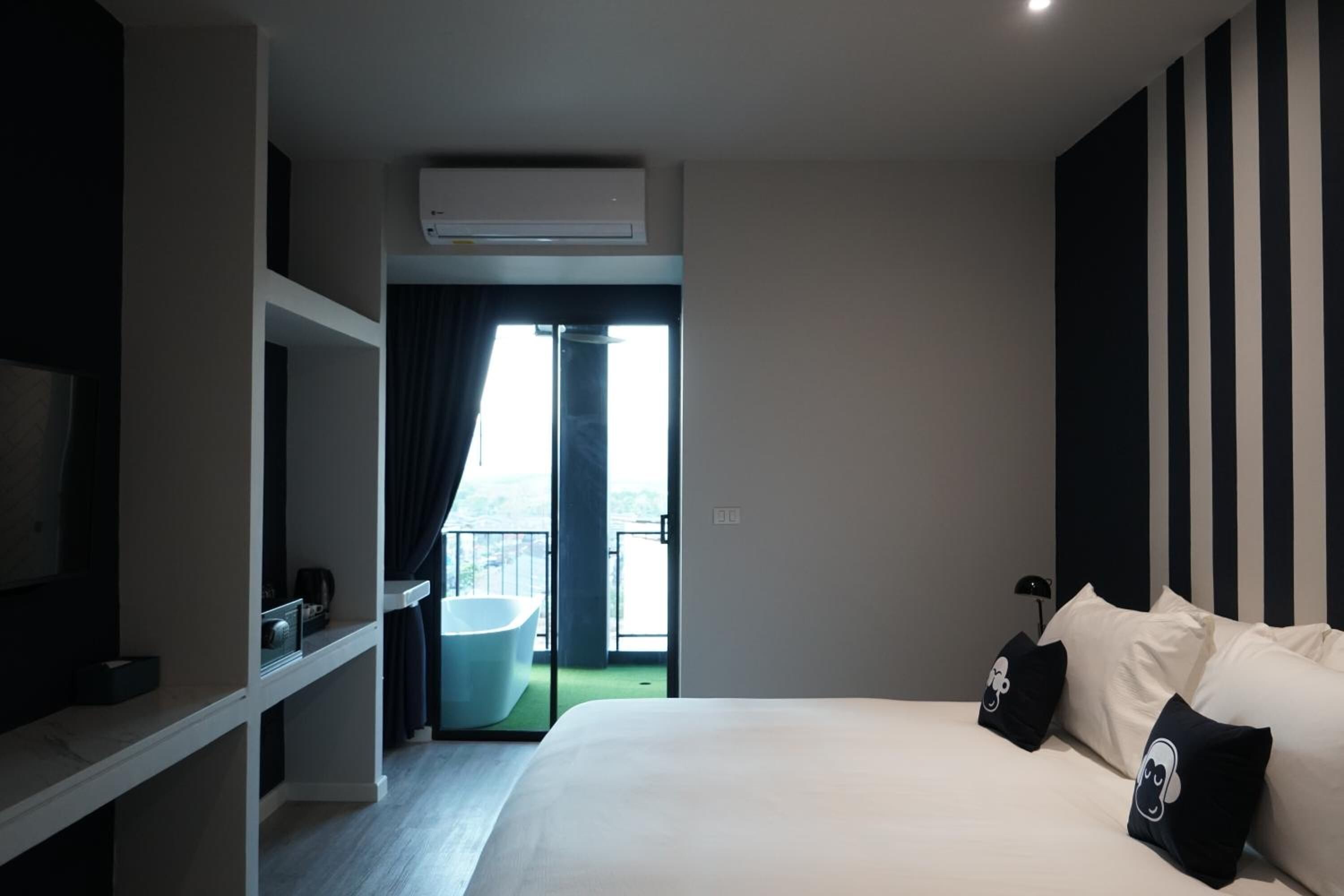 A modern hotel room with a large bed, a built-in TV, a balcony with a view, and a separate bathroom with a bathtub.