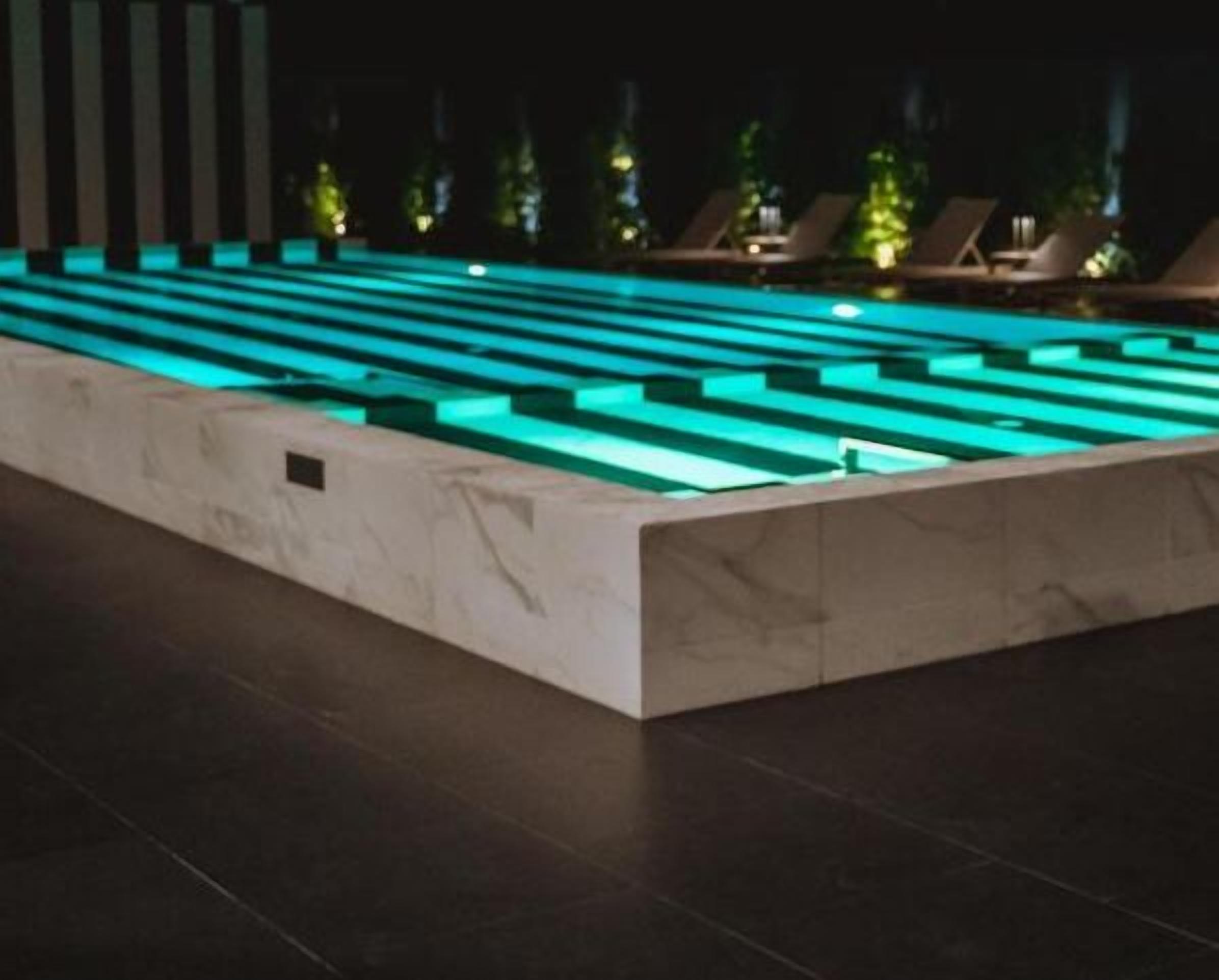 Une piscine au design géométrique, entourée de chaises longues et dotée d’un fond sombre.