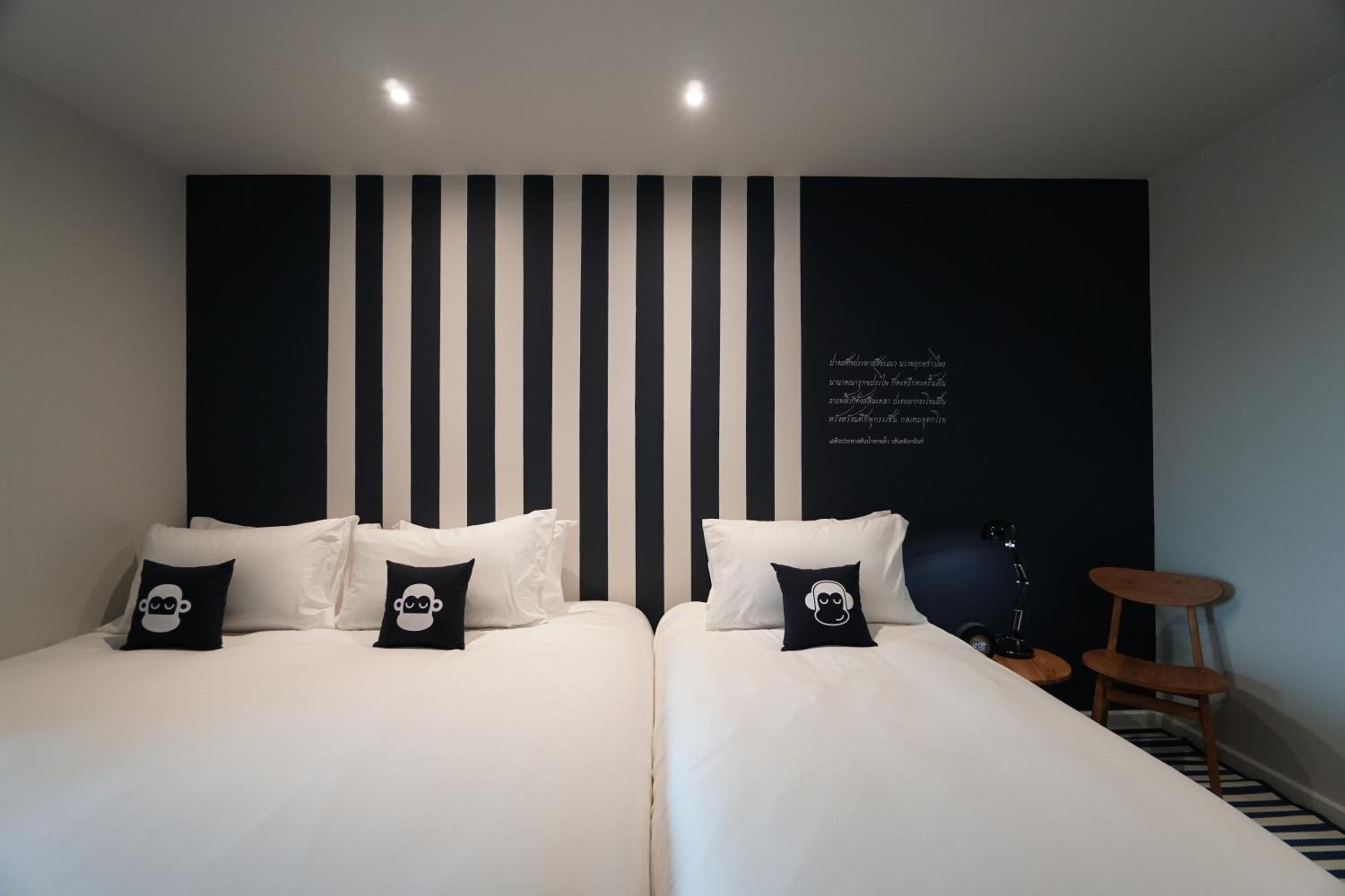A hotel room with two beds, black and white striped headboard, and a small side table with a lamp.