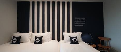A hotel room with two beds, black and white striped headboard, and a small side table with a lamp.