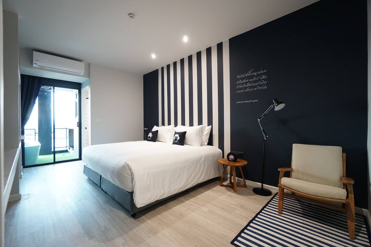 Ein modernes Hotelzimmer mit einem großen Bett, einem Sessel, einem Schreibtisch und einer Wand mit vertikalen Streifen.