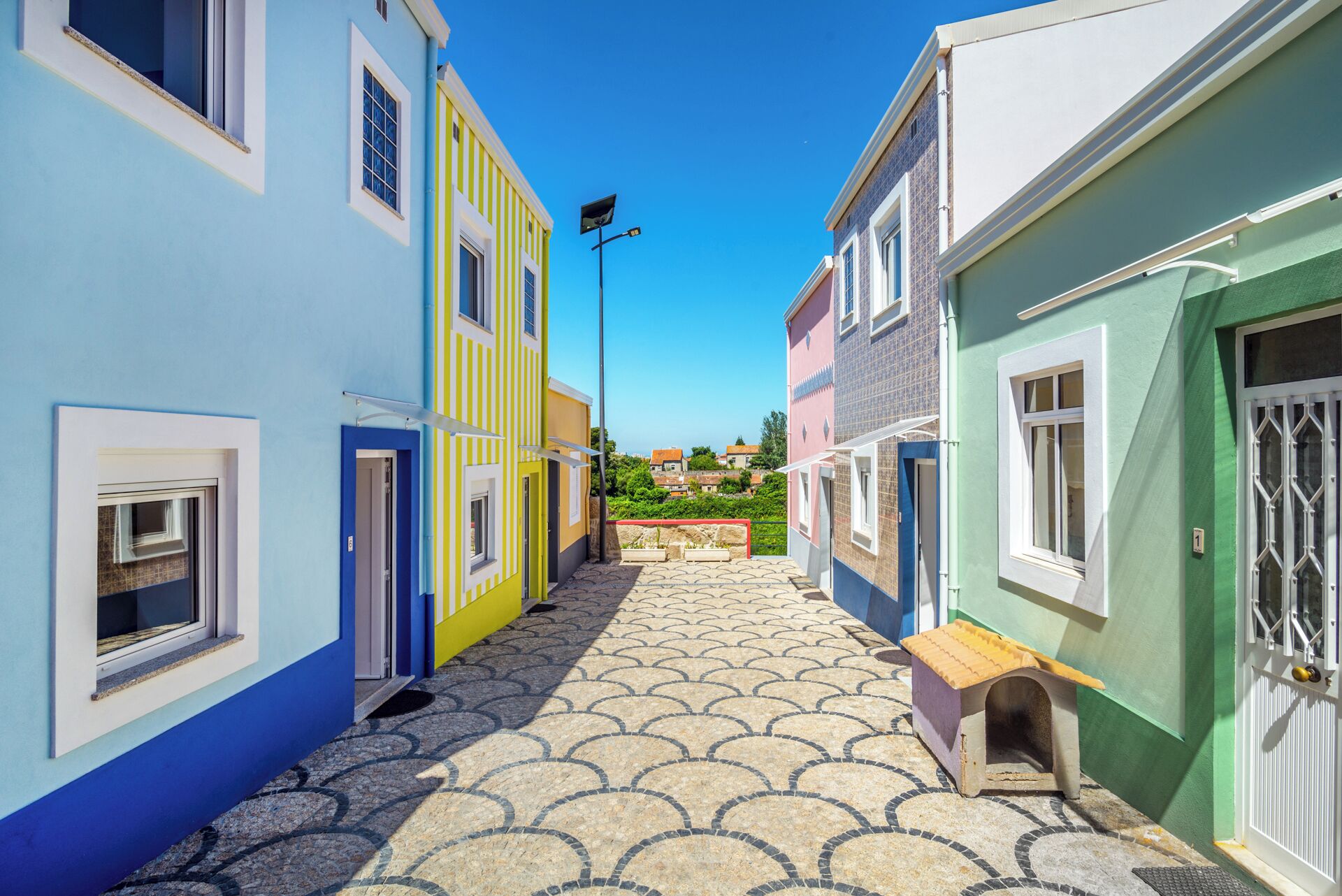 A narrow street with colorful buildings, a clear sky, and a tiled pavement.