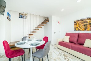 Zona pranzo con tavolo rotondo, sedie rosse e grigie, una scala con gradini in legno e un divano rosso.