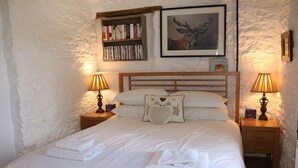 A neatly made bed with white linens and towels, a wooden headboard, and two bedside tables with lamps. A bookshelf and a framed picture are on the wall above the bed. - Keepers Cottage - Cosy Peak District Retreat (Derbyshire)