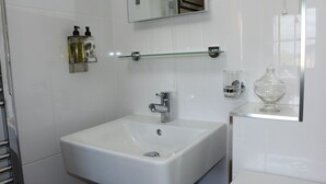 A bathroom with a white sink, a mirror, a glass shelf, and a glass container. - Keepers Cottage - Cosy Peak District Retreat (Derbyshire)
