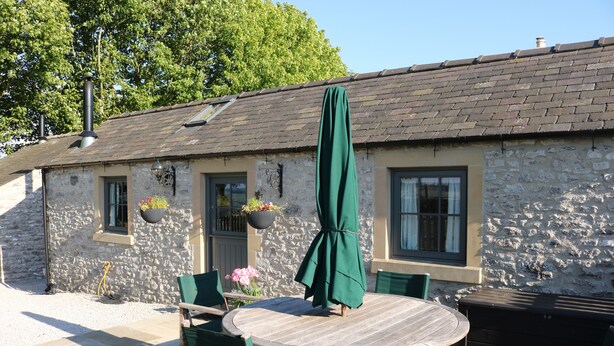 A stone building with a tiled roof, a round wooden table with chairs, and a green umbrella. - Keepers Cottage - Cosy Peak District Retreat (Derbyshire)
