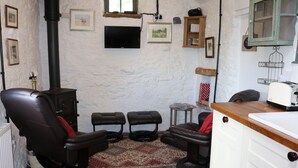 A rustic room with a fireplace, a television, and a kitchen area. - Keepers Cottage - Cosy Peak District Retreat (Derbyshire)