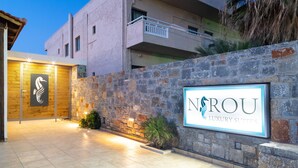 A modern building with a stone facade, a wooden entrance, and a sign for 'NROU Luxury Suites'. - Wave Suite By the Sea (Hersonissos)