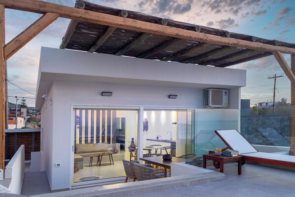 A modern outdoor living space with a glass door leading to an interior area, a wooden pergola, and a lounge chair. - Wave Suite By the Sea (Hersonissos)