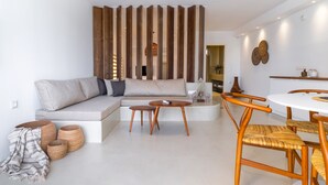 A modern living room with a sectional sofa, a round coffee table, and a dining table with chairs. There are woven baskets and a striped throw blanket on the floor. - Wave Suite By the Sea (Hersonissos)