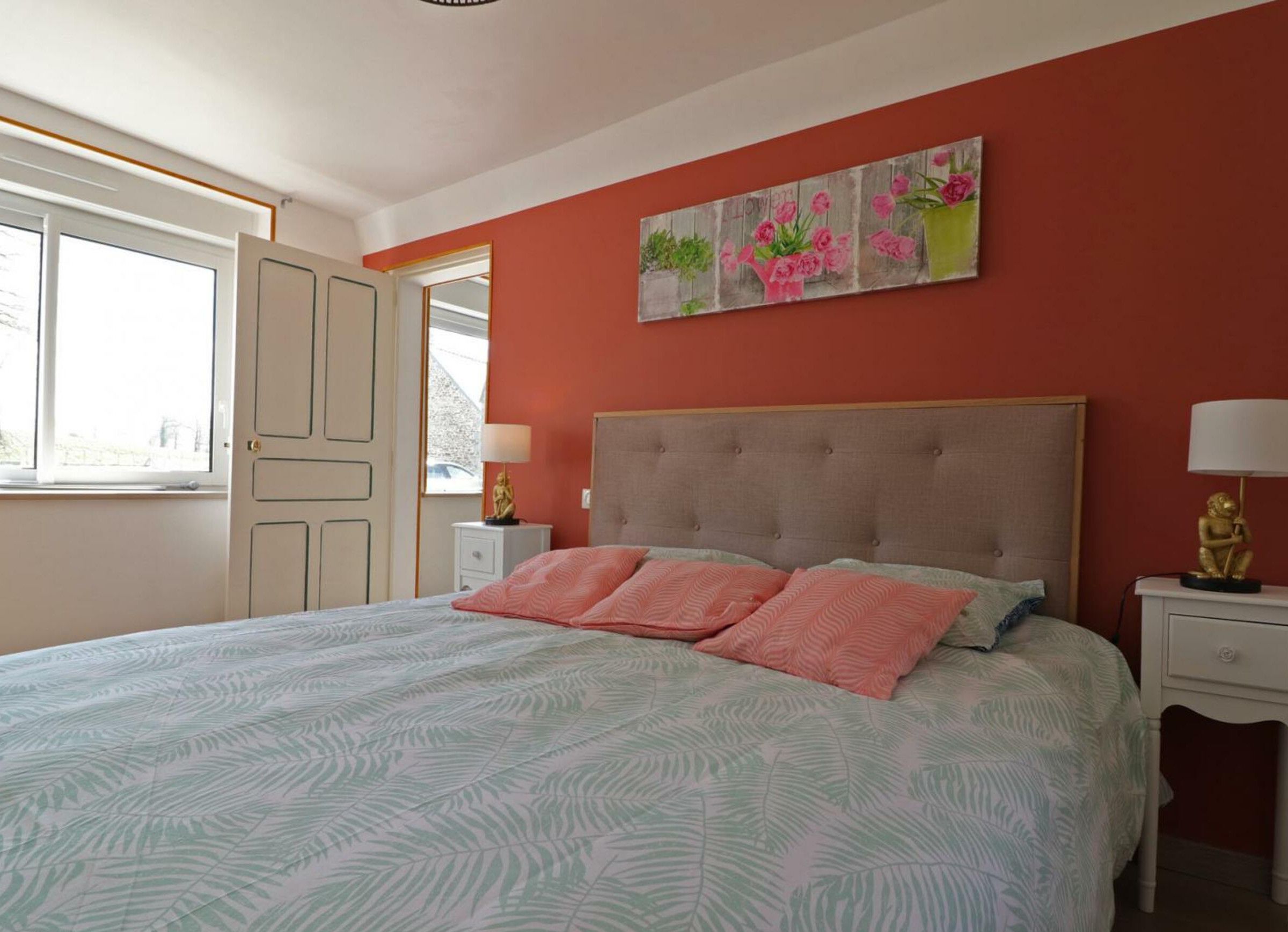 A bedroom with a bed, a nightstand, a lamp, a painting, and a window.