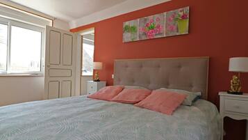 A bedroom with a bed, a nightstand, a lamp, a painting, and a window.