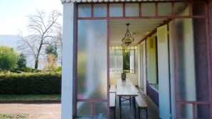 Un espace extérieur abrité, doté d’une table et de bancs, entouré de panneaux en verre dépoli et d’une rambarde en métal.