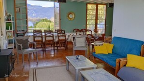 Un salon chaleureux avec un canapé bleu, des chaises en bois, une table à manger et une vue sur les montagnes par de grandes fenêtres ouvertes.