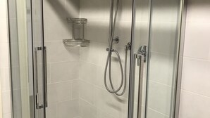 En moderne bruseniche med glasvægge, et håndbruserhoved og et loftmonteret regnbruser.