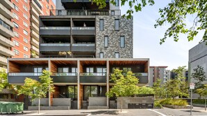 Ein mehrstöckiges Gebäude mit moderner Architektur, mit Balkonen, einem Parkplatz und umliegender Bepflanzung.