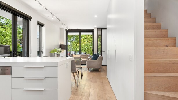 Eine moderne Küche mit einer zentralen Kochinsel, einem Essbereich mit Stühlen und einer Treppe, die in eine obere Etage führt.