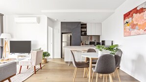 Eine moderne Küche mit weißen Schränken, einem eingebauten Backofen und einer Essecke mit einem runden Tisch und grauen Stühlen.