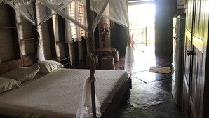 Ein Zimmer mit einem Himmelbett, einem Holzschrank und einem Ventilator.