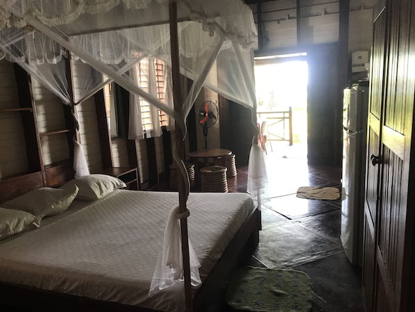 Una habitación con una cama con dosel, un armario de madera y un ventilador.