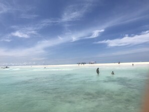 A beach with clear turquoise water, a sandy shore, and a few people in the distance.