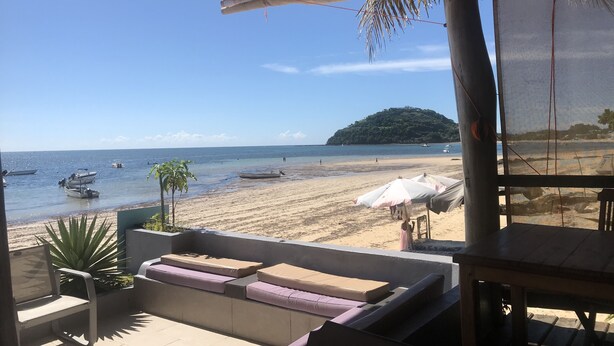 Blick auf einen Strand von einer überdachten Sitzgelegenheit mit Kissen und Tisch.