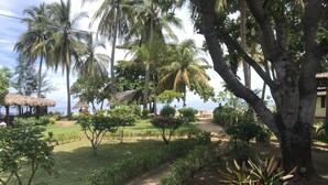 Ein tropischer Garten mit Palmen, einer strohgedeckten Hütte und einem Feldweg, der zum Strand führt.