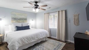 Quarto com cama, ventoinha no teto, janela com cortinas e uma decoração de macramé na parede.