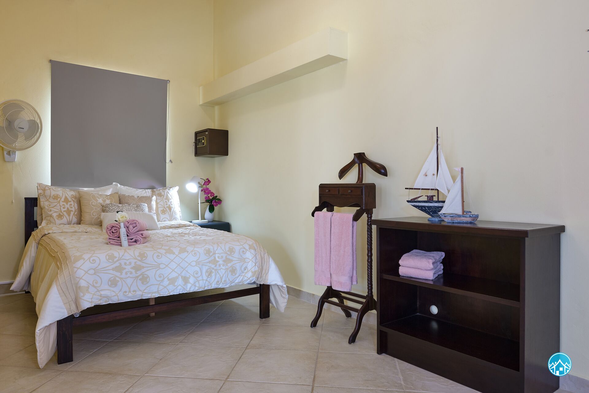 Un dormitorio con cama, mesita de noche, lámpara y una estantería con un modelo de velero.