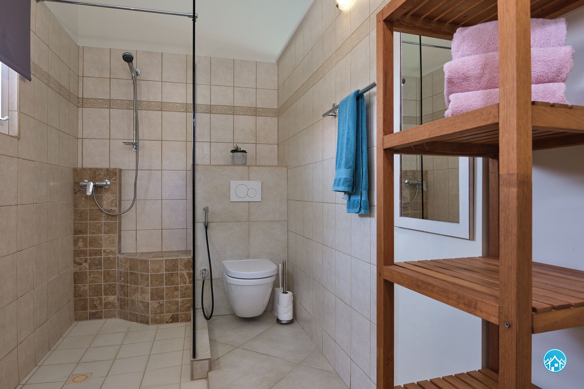 Une salle de bain avec une douche, des toilettes et une étagère en bois où sont rangées les serviettes.