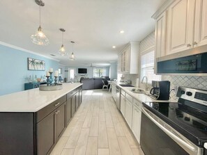 A modern kitchen with a large island, white cabinetry, and stainless steel appliances. - Searenity Escape - New Pool, Bikes, Parking, Near the Beach (Naples)