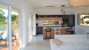 A modern kitchen with a central island, bar stools, and a dining area with a white sofa.