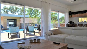 A modern living room with a white sofa, a wooden coffee table, and a pool view.