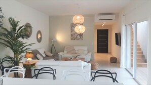 A modern living room with a sofa, chairs, a coffee table, and a large plant. There is a staircase leading to another level.