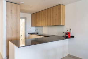 A modern kitchen with wooden cabinets, a stainless steel countertop, and a red kettle.