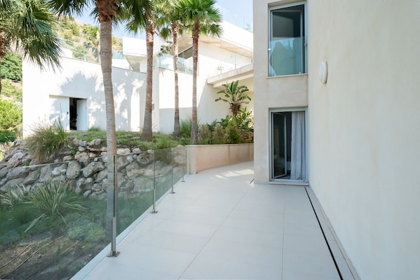 A modern building with a glass balcony, palm trees, and a stone wall.