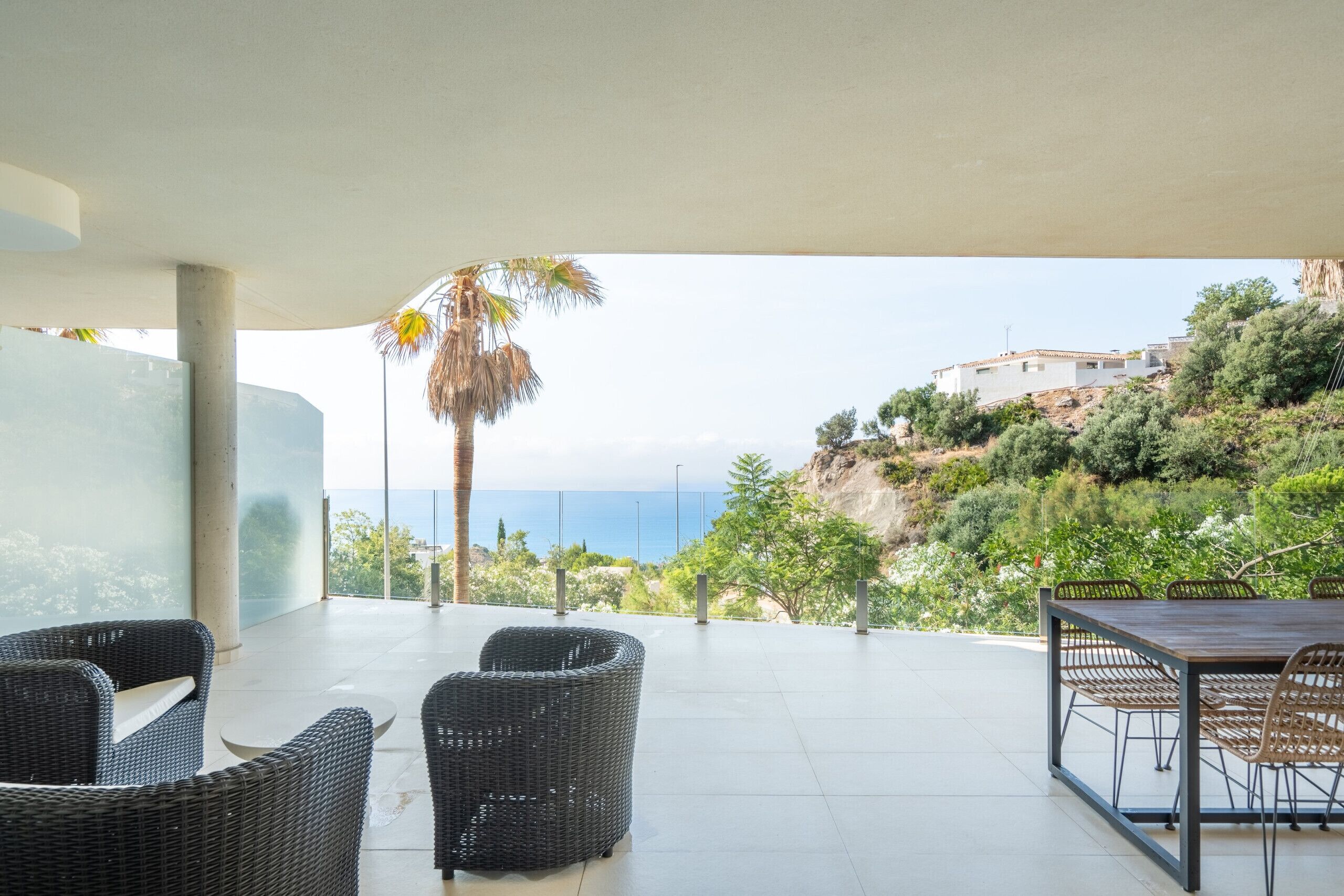 Una terraza con muebles de mimbre, una mesa y vistas al mar y las colinas.