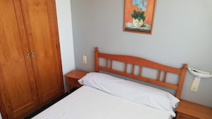 Une chambre à coucher avec un lit en bois, une table de chevet, une armoire en bois et un luminaire fixé au mur.