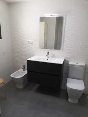 A modern bathroom with a white sink, bidet, and toilet.