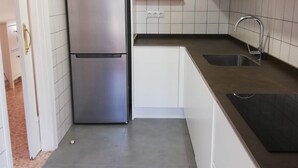 Kompakti keittiö, jossa on valkoiset kaapit, ruostumattomasta teräksestä valmistettu jääkaappi, pesuallas ja laatoitettu välitila.