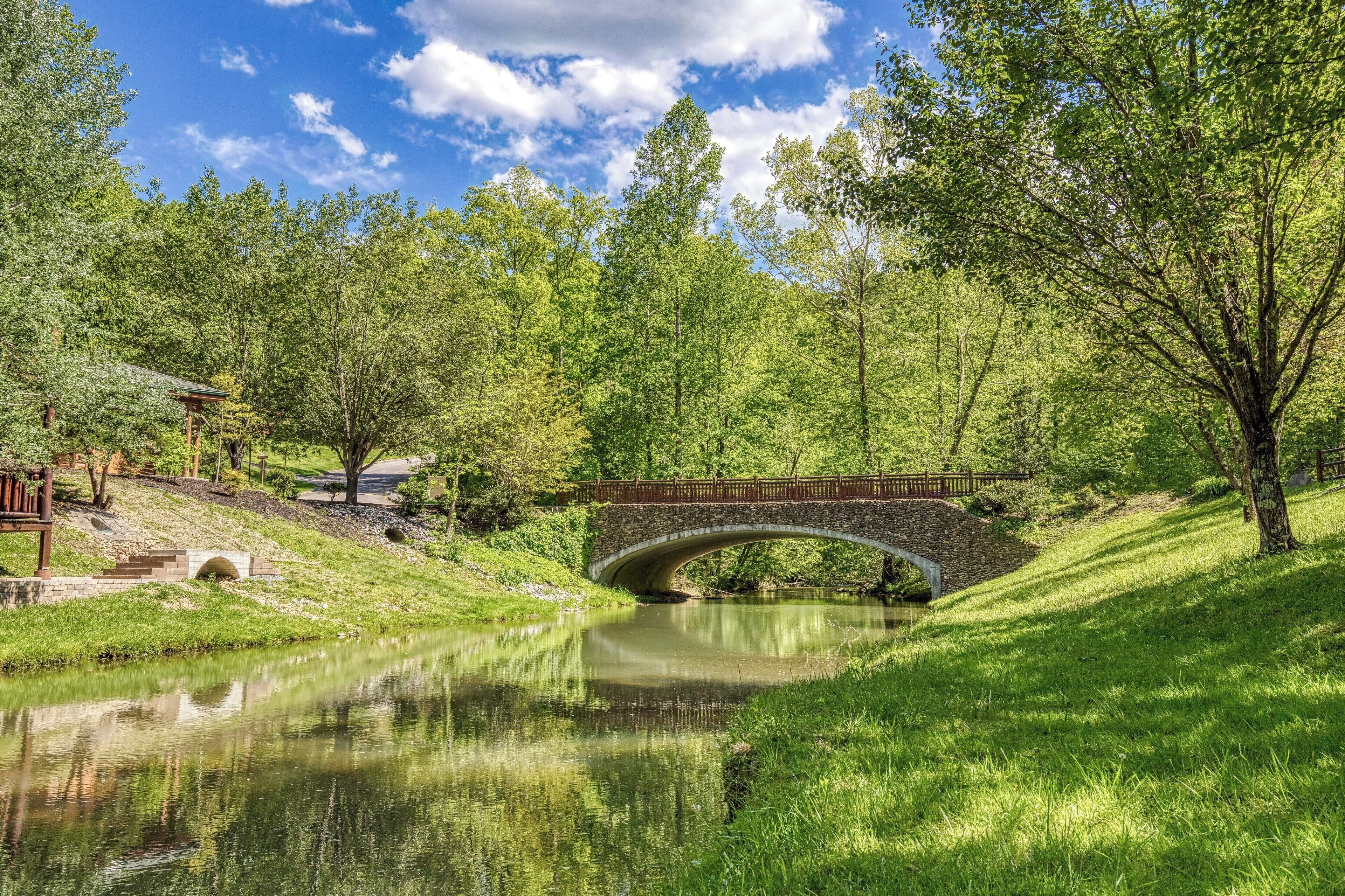 Un pont de pierre enjambant une rivière paisible, entouré d’une végétation luxuriante et d’arbres.