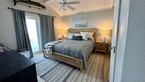 A bedroom with a bed, two bedside tables, a ceiling fan, a large fish mounted on the wall, and a view of the outdoors through a sliding door.