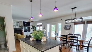 A spacious kitchen with a central island, pendant lighting, and a dining area with wooden chairs and a table.