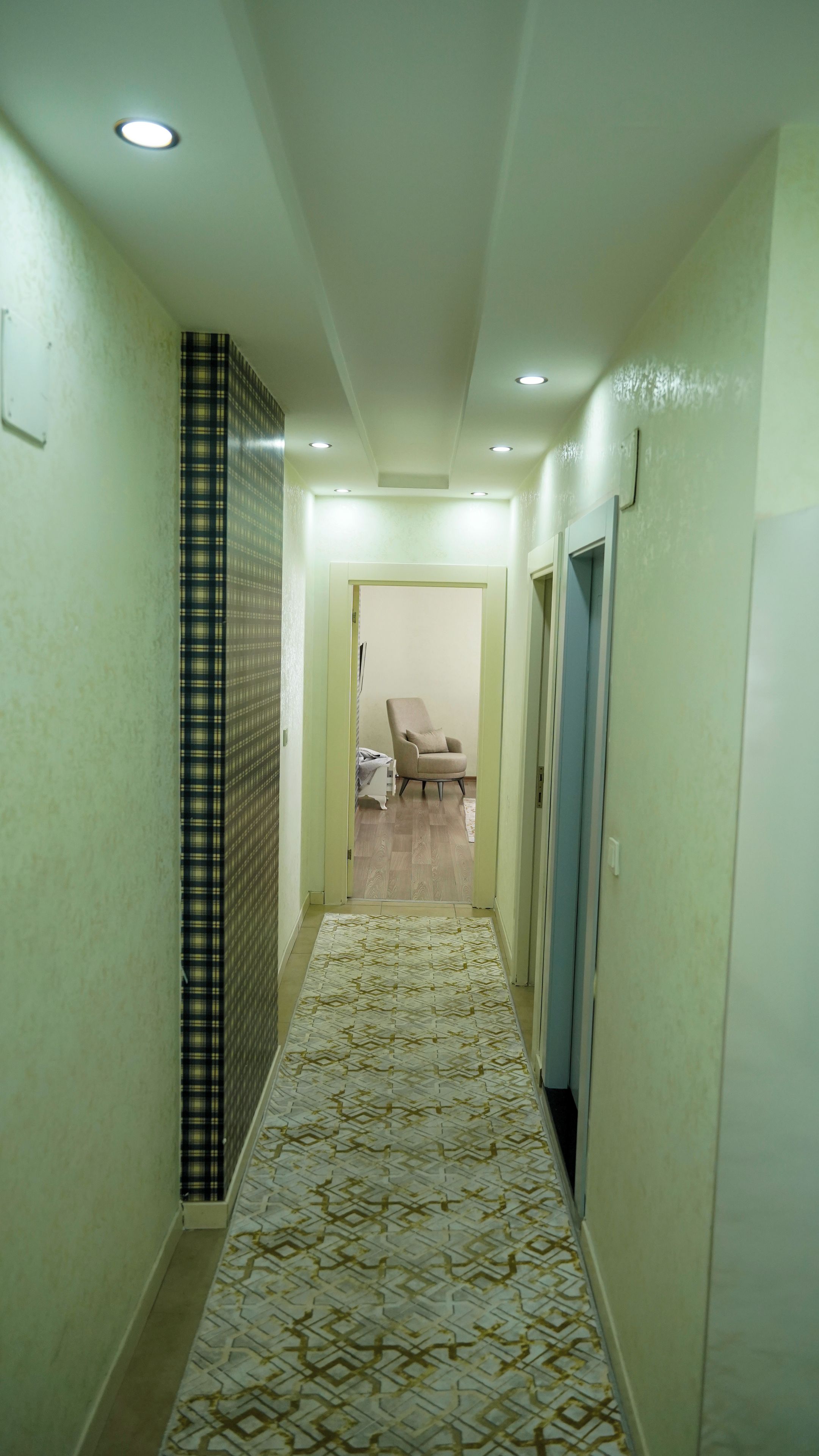 A hallway with patterned flooring, a chair, and doors leading to other rooms.