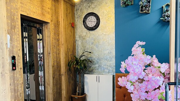 A hallway with a wooden door, a clock, a potted plant, and a pink flowering plant.