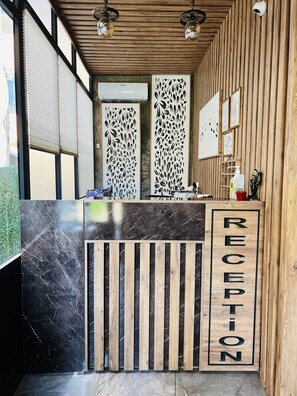 Un comptoir d’accueil avec un plateau en marbre noir et des lattes en bois, un mur en bois avec des lattes verticales et une caméra de surveillance.