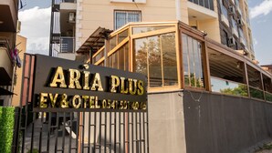 A multi-story building with balconies, a sign for 'ARIA PLUS EV & HOTEL', and a gated entrance.