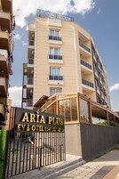 Un edificio de varios pisos con balcones, un cartel que dice 'ARIA PLUS EV & HOTEL' y una entrada portonada.