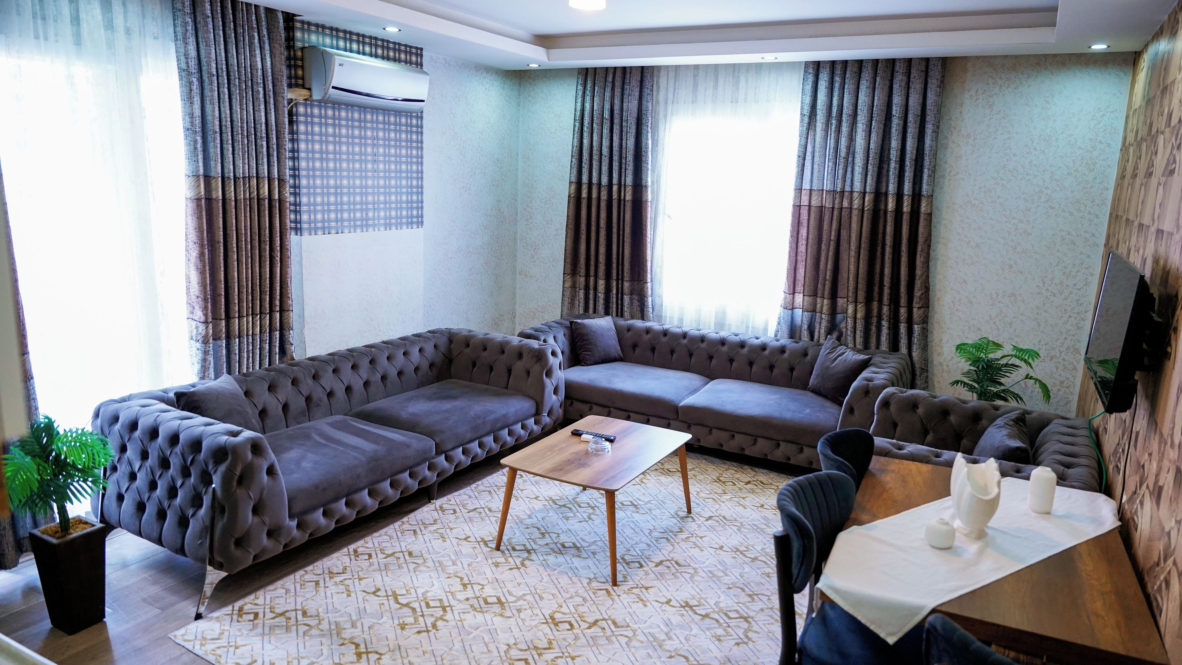 Ein Wohnzimmer mit einer Eckcouch, einem Couchtisch und einem an der Wand befestigten Fernseher.